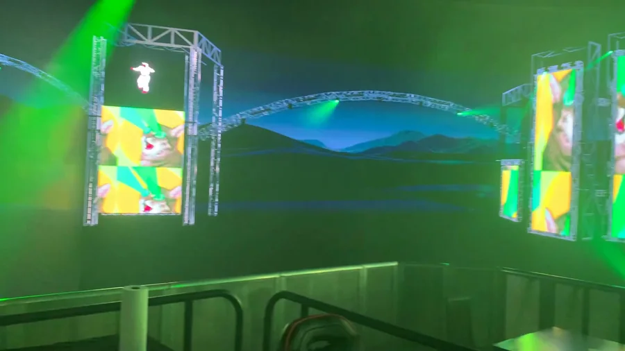 Side view of the virtual stage showing colorful LED walls, rails, and blue landscape environment