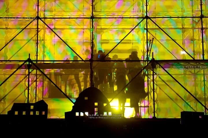 Backlit performers silhouetted behind the Tower of Babel projection surface