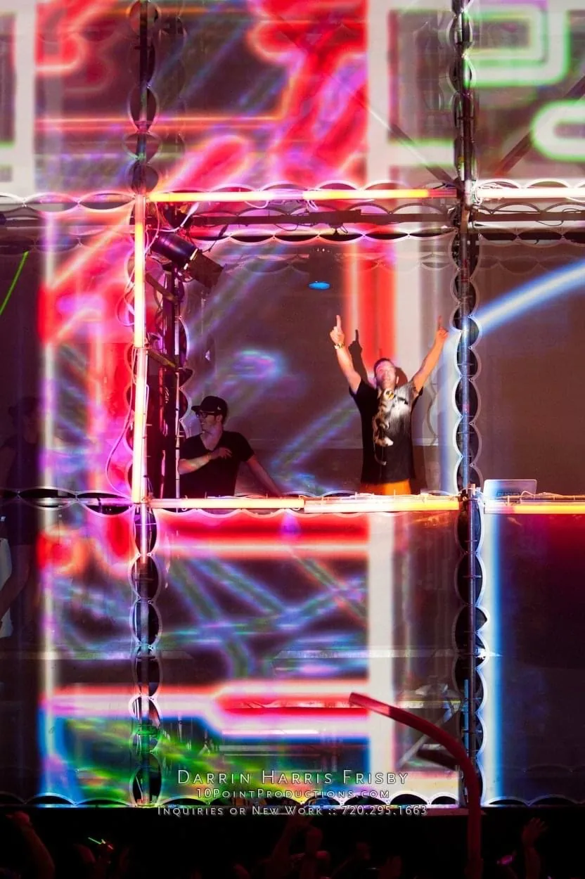 DJs performing inside the Tower of Babel booth with vivid projection mapping across the scaffold