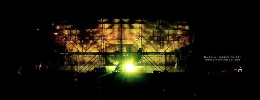 Distant night view of the Tower of Babel stage with a bright central light and mapped facade