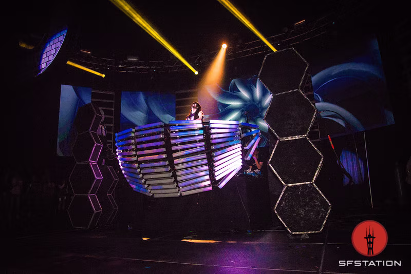 Steve Aoki performing inside the illuminated booth with synchronized blue visuals across hexagonal screens