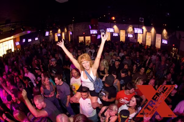 Crowd member with arms raised during the live band and visual show at XTREME